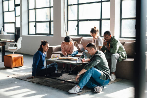 A diverse group of young professionals or students engage in collaboration and discussion in a bright, contemporary co-working environment.