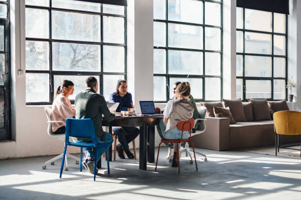 Group of young adults engaging in project discussions in a bright co-working environment with stylish interior.